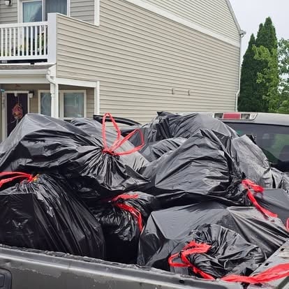 Pickup truck bed filled with black garbage bags secured with red bungee cords in residential driveway