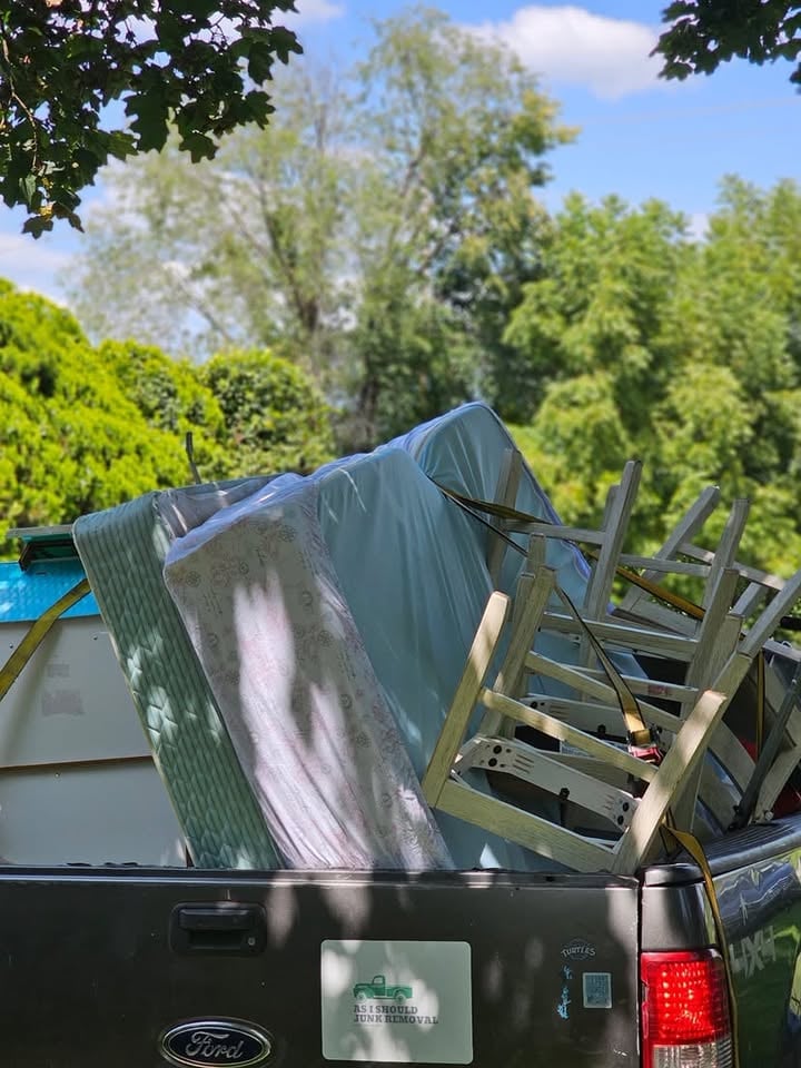 Ford truck bed loaded with roofing shingles and wooden ladder rack on sunny day with trees in background